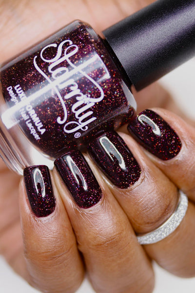 Protostar by Starrily, deep red-brown holographic with copper micro glitter flaring gold-copper under direct flash, bottle held in a medium-deep hand