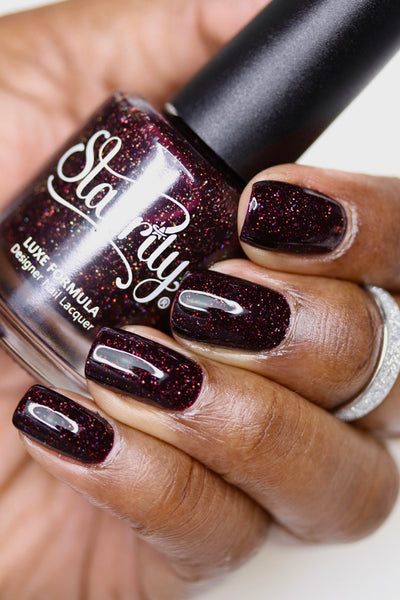 Protostar by Starrily, deep red-brown holographic base with copper and burgundy micro glitter sparkle in studio light, bottle held in a deep hand