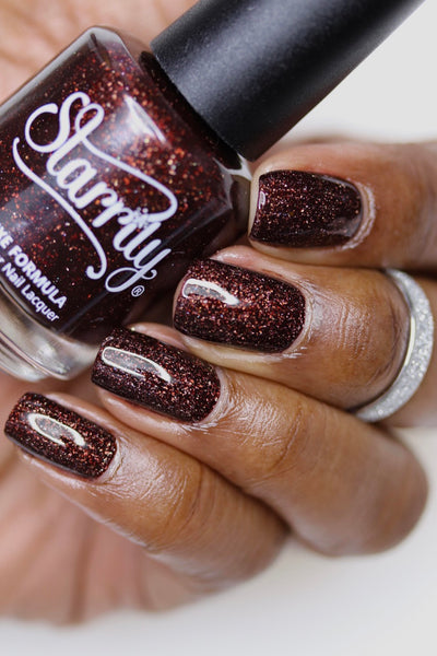 Into The Woods by Starrily, dark brown holographic showing warm copper-red scattered holo flakes in studio light, bottle held in a deep skin tone hand