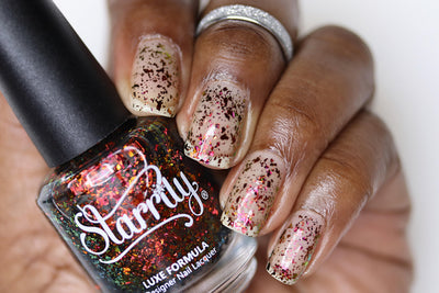 Crunchy Leaves by Starrily, gold-green multichrome flakie topper showing orange-to-deep-green flake shift over sheer nude base, bottle held in a deep skin tone hand